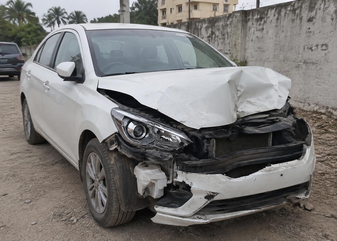 Accidental white sedan with a damaged front end in an Ahmedabad yard